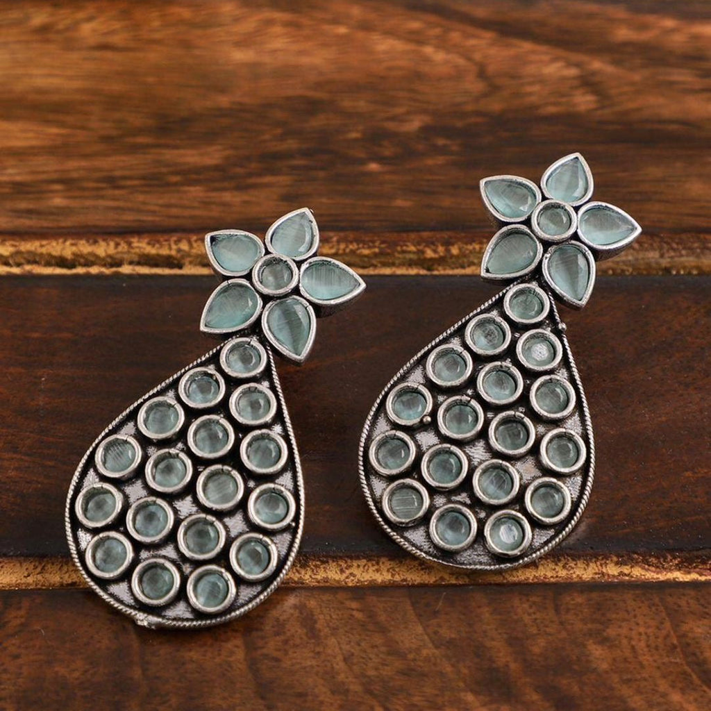 Pair of silver and green teardrop-shaped earrings on a wooden surface