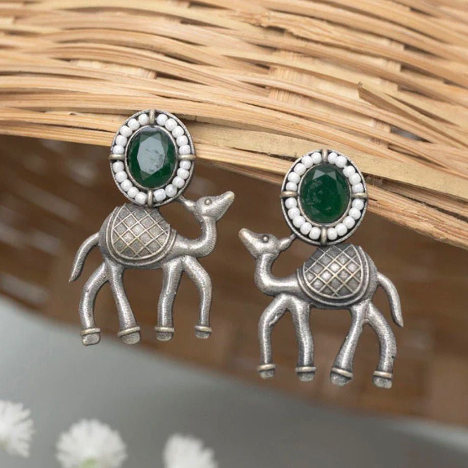 Silver camel-shaped earrings with green gemstones on a natural background