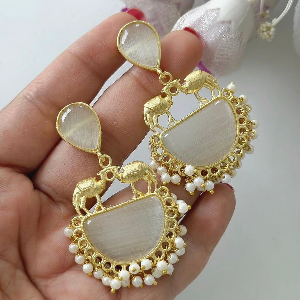 Gold and pearl earrings held in a hand with a light background