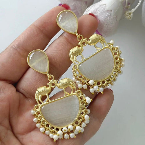 Gold and pearl earrings held in a hand with a light background