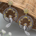 Silver earrings with bird and floral designs on a woven surface
