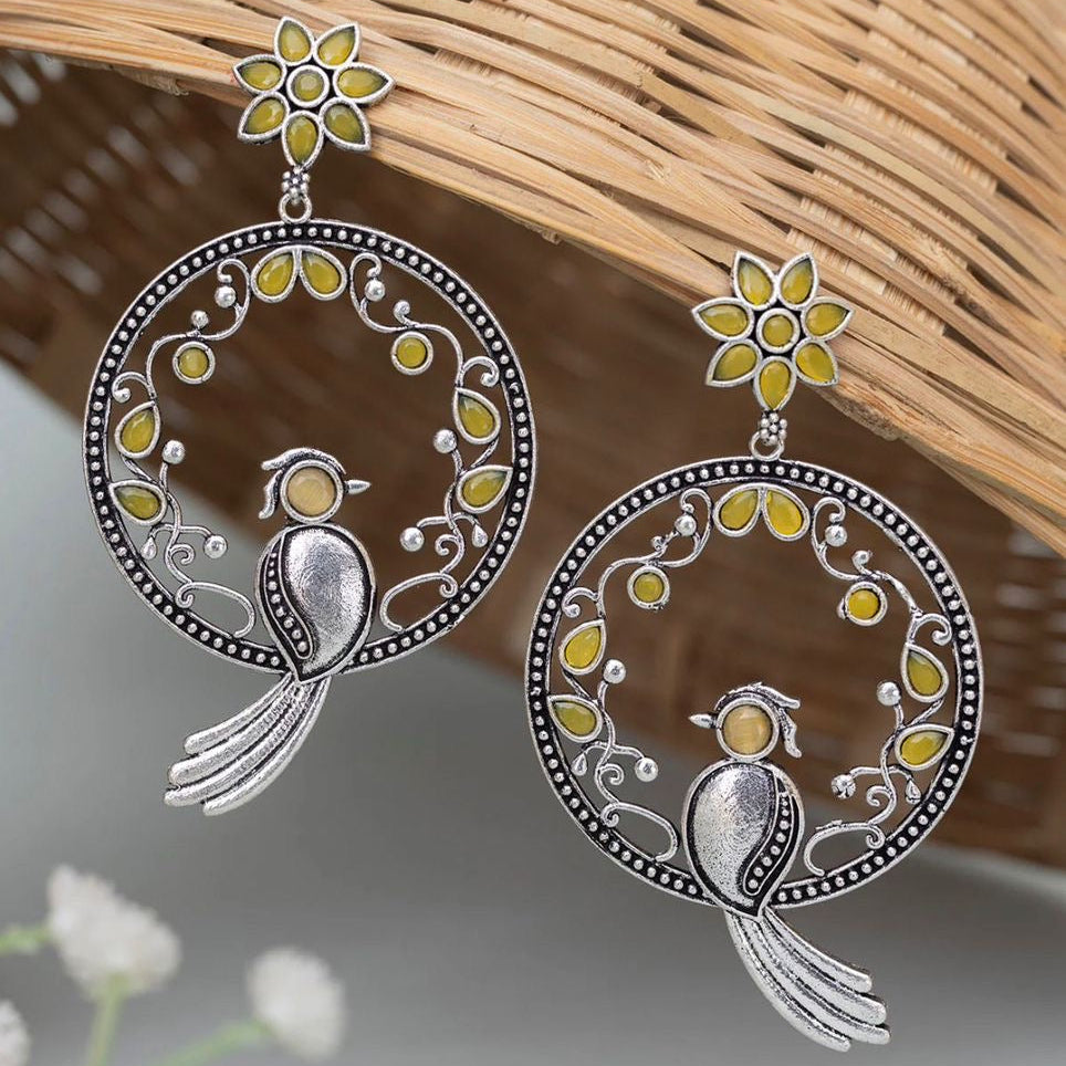 Silver earrings with bird and floral designs on a woven surface
