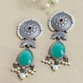 Ornate earrings with turquoise stones and pearl accents on a beige background