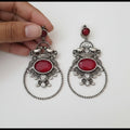 Ornate silver earrings with red stones held by a hand on a white surface.